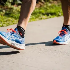 Course à pied avec des chaussures bleues et oranges. Le pied gauche montre une légère pronation, typique d'une foulée naturelle.