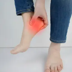 Main d'une personne touchant son talon, zone rouge indiquant une douleur. Peut-être une douleur talon course à pied.