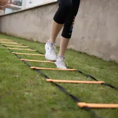 Une personne effectue un exercice lombaire sur une échelle d'agilité dans l'herbe.