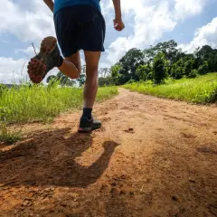 Un coureur s'élance sur un chemin de terre bordé d'herbes hautes, prêt pour un trail longue distance sous un ciel nuageux.