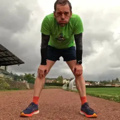 Un coureur fatigué, penché en avant sur une piste d'athlétisme, se prépare pour la récupération course à pied. Le ciel est couvert.