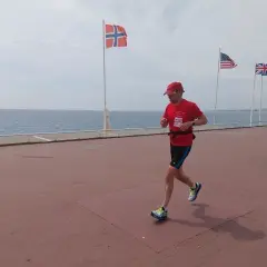 Un homme court sur la promenade des Anglais à Nice, drapeau norvégien et américain en arrière-plan.