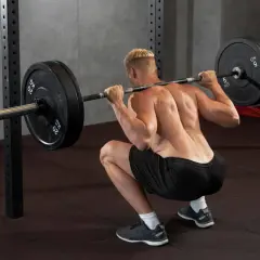 Un homme réalise un squat avec une barre chargée dans une salle de sport. Ce mouvement de squat sport est essentiel pour le développement musculaire.