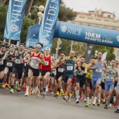 Des coureurs s'élancent sous une arche bleue lors du semi-marathon de Nice. Les numéros de dossard sont visibles.