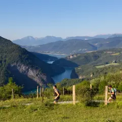 Deux coureurs s'élancent sur le sentier du maratrail des passerelles, dominant un lac bleu entouré de montagnes verdoyantes.