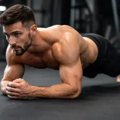 Un homme musclé maintient une position de gainage ventre, concentré sur son entraînement en salle de sport.