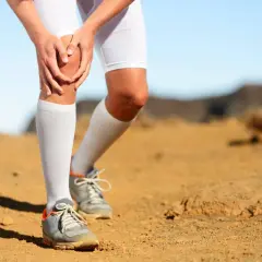 Coureur à pied tenant son genou, souffrant de douleur. Le paysage désertique suggère un effort intense.
