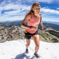 Une coureuse en plein effort, le visage rayonnant, dévale une pente enneigée en montagne. Son **endurance active** est mise à l'épreuve dans ce paysage spectaculaire.