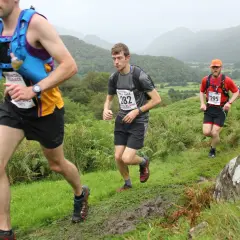 Coureurs en pleine course sur un sentier boueux, dans le cadre du trail des rois maudits. Paysage vallonné et brumeux.