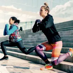 Deux femmes font des fentes sur des escaliers extérieurs, profitant d'une séance de ppg sport sous un ciel bleu.