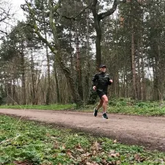 Un homme en tenue de sport ef running sur un sentier forestier, entouré d'arbres.