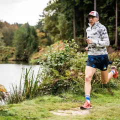 Un athlète court près d'un lac, dans une forêt. Il pourrait s'entraîner pour courir à Nantes.