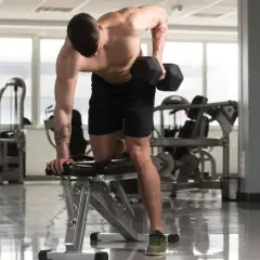 Un homme musclé effectue un exercice haltère, concentré sur son entraînement dans une salle de sport lumineuse.