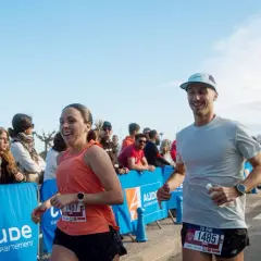 Un couple court joyeusement lors d'un marathon, le soleil brille sur la côte indigo.