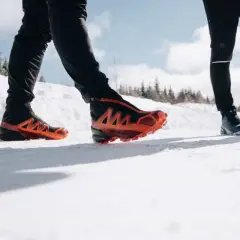 Deux personnes en chaussures de trail, l'une avec des chaussures orange vif, parcourent un sentier enneigé du Haut Giffre.