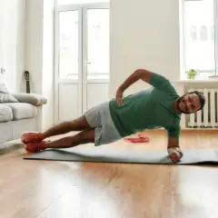 Un homme souriant pratique le gainage latéral sur un tapis de yoga dans son salon.
