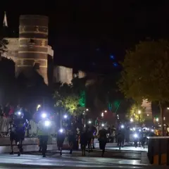 Courseurs illuminés par des lampes frontales, traversant la ville pour le trail de l'apocalypse, avec un château en arrière-plan.