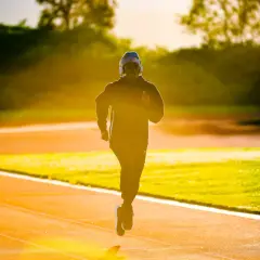 Un jeune homme court sur une piste d'athlétisme à Lyon, baigné par la lumière dorée du soleil couchant.