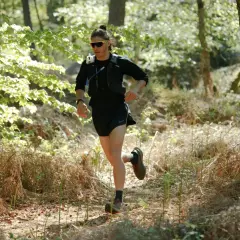 Un coureur s'entraîne dans une forêt ensoleillée, prêt à courir avant une course.