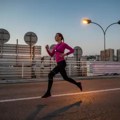 Une femme en tenue de sport rose et noire court sur une route au crépuscule, profitant d'une course de nuit sous les lampadaires.