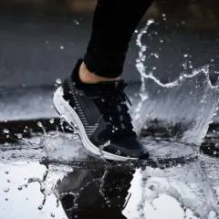Un pied en basket noir et blanc éclabousse l'eau en courant sous la pluie.
