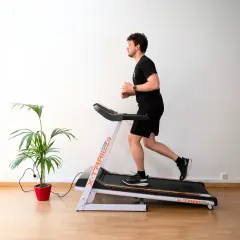 Un homme court sur un tapis de course, suivant un programme d'entraînement. Une plante verte décore la pièce.