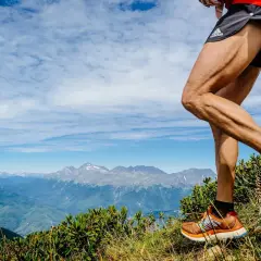 Un coureur en plein entrainement trail, jambes musclées, sur un sentier de montagne avec un panorama spectaculaire.
