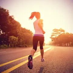 Une coureuse en plein entraînement fartlek, variant son allure sur une route bordée d'arbres au lever du soleil.