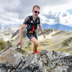 Un traileur en plein effort sur un sentier rocailleux, le regard déterminé, incarne l'ultra spirit dans un paysage montagneux spectaculaire.