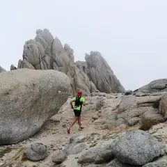 Un coureur en tenue de trail suit le sentier balisé PR-M1, traversant un paysage rocheux et brumeux.