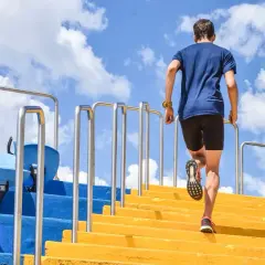 Un homme monte des marches jaunes, un entraînement efficace pour les meilleurs exercices pour les jambes. Le ciel bleu et les nuages sont visibles.