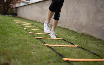 Une personne effectue un exercice lombaire sur une échelle d'agilité dans l'herbe.