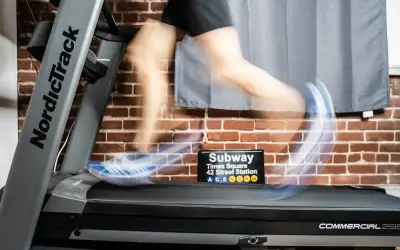 Person en mouvement sur un tapis roulant NordicTrack, simulant des gammes athlétiques. Un panneau "Subway Times Square" est visible.