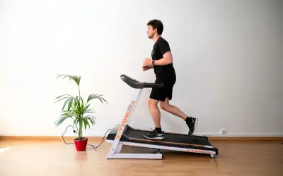Un homme court sur un tapis de course, suivant un programme d'entraînement. Une plante verte décore la pièce.