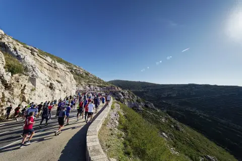 Course de running sur une route côtière, avec un grand groupe de coureurs affrontant le dénivelé Marseille Cassis sous un ciel bleu éclatant.