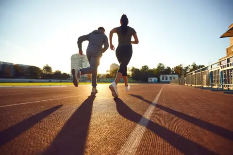 Deux coureurs sur une piste, le soleil couchant projette leurs ombres. Ils s'entraînent, peut-être pour savoir que veut dire EF en course à pied.