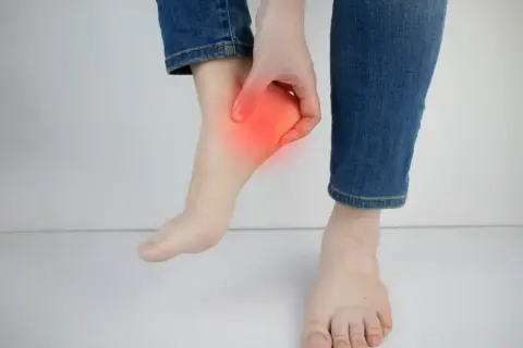Main d'une personne touchant son talon, zone rouge indiquant une douleur. Peut-être une douleur talon course à pied.