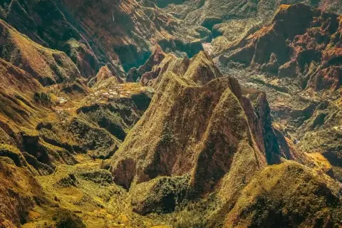 Paysage spectaculaire de montagnes verdoyantes et escarpées, rappelant les défis de la diagonale des fous. Des villages sont nichés dans les vallées.