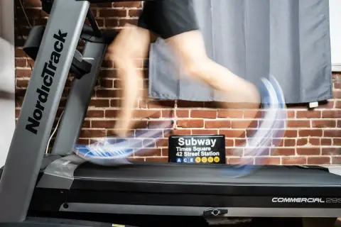 Person en mouvement sur un tapis roulant NordicTrack, simulant des gammes athlétiques. Un panneau "Subway Times Square" est visible.