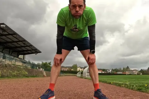 Un coureur fatigué, penché en avant sur une piste d'athlétisme, se prépare pour la récupération course à pied. Le ciel est couvert.