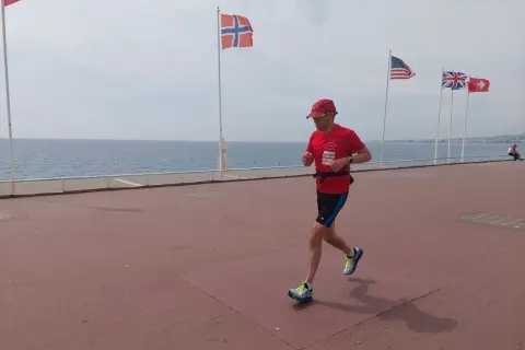 Un homme court sur la promenade des Anglais à Nice, drapeau norvégien et américain en arrière-plan.