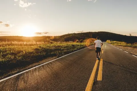 Un homme court sur un **road run trail** au coucher du soleil, profitant de la nature et de la lumière dorée.