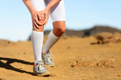 Coureur à pied tenant son genou, souffrant de douleur. Le paysage désertique suggère un effort intense.