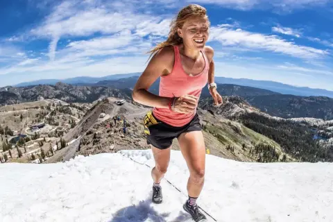 Une coureuse en plein effort, le visage rayonnant, dévale une pente enneigée en montagne. Son **endurance active** est mise à l'épreuve dans ce paysage spectaculaire.