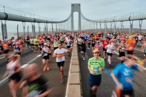 Des coureurs franchissent le pont, affrontant le dénivelé du marathon de New York. Le ciel est couvert, mais l'énergie est palpable.