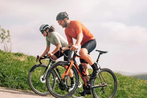 Deux cyclistes en plein **entrainement croisé** sur une route de campagne, profitant du paysage verdoyant sous un ciel nuageux.