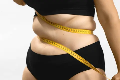 Une femme mesure son tour de taille avec un mètre ruban jaune, symbolisant le suivi du pourcentage masse grasse et le parcours de perte de poids.