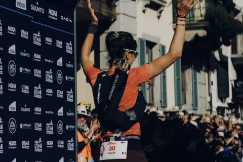 Coureuse célébrant sa victoire à l'UTMB, portant son sac d'hydratation et le matériel obligatoire.