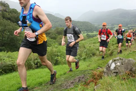 Coureurs en pleine course sur un sentier boueux, dans le cadre du trail des rois maudits. Paysage vallonné et brumeux.