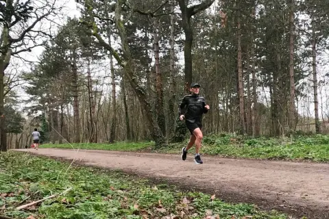 Un homme en tenue de sport ef running sur un sentier forestier, entouré d'arbres.
